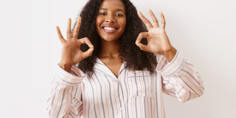 Positive human emotions, feelings and facial expressions. Attractive joyful African girl with voluminous hairstyle and radiant broad smile, showing ok gesture, connecting thumb and fore finger